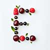 Letter E english alphabet in the form of a pattern of natural organic berries - ripe fresh raspberry, black currant, cherry, green mint leaf isolated on a white background. Top view.