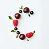 Letter C english alphabet in the form of a pattern of natural organic berries - ripe fresh raspberry, black currant, cherry, green mint leaf isolated on a white background. Top view.