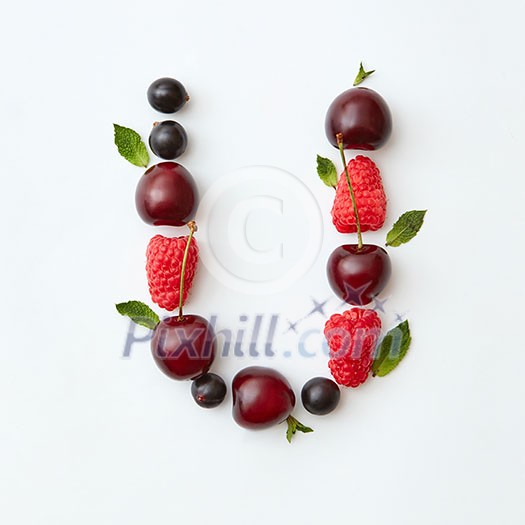Letter U english alphabet in the form of a pattern of natural organic berries - ripe fresh raspberry, black currant, cherry, green mint leaf isolated on a white background. Top view. Letter U english alphabet in the form of a pattern of natural organic berries - ripe fresh raspberry, black currant, cherry, green mint leaf isolated on a white background. Top view.
