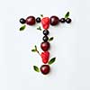 Letter T english alphabet in the form of a pattern of natural organic berries - ripe fresh raspberry, black currant, cherry, green mint leaf isolated on a white background. Top view.
