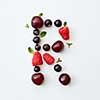 Letter R english alphabet in the form of a pattern of natural organic berries - ripe fresh raspberry, black currant, cherry, green mint leaf isolated on a white background. Flat lay