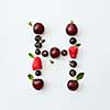 Letter H english alphabet in the form of a pattern of natural organic berries - ripe fresh raspberry, black currant, cherry, green mint leaf isolated on a white background. Top view.