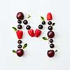 Letter M english alphabet in the form of a pattern of natural organic berries - ripe fresh raspberry, black currant, cherry, green mint leaf isolated on a white background. Top view.