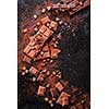 Broken chocolate pieces and cocoa powder on marble. The chunks of chocolate over dark background