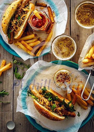 Delicious fresh hot dogs in homemade buns with arugula and ketchup, with beer and French fries on a wooden background Delicious fresh hot dogs in homemade buns with arugula and ketchup, with beer and French fries on a wooden background