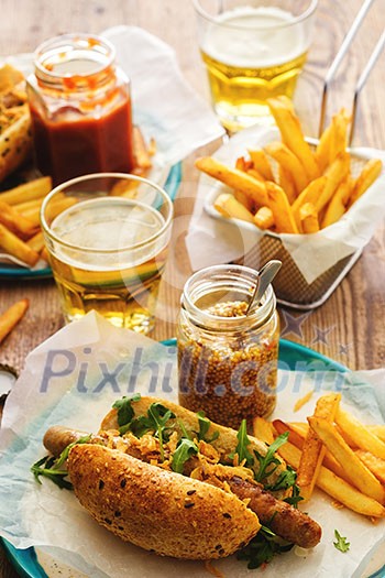 Delicious fresh hot dogs in homemade buns with arugula and ketchup, with beer and French fries on a wooden background Delicious fresh hot dogs in homemade buns with arugula and ketchup, with beer and French fries on a wooden background