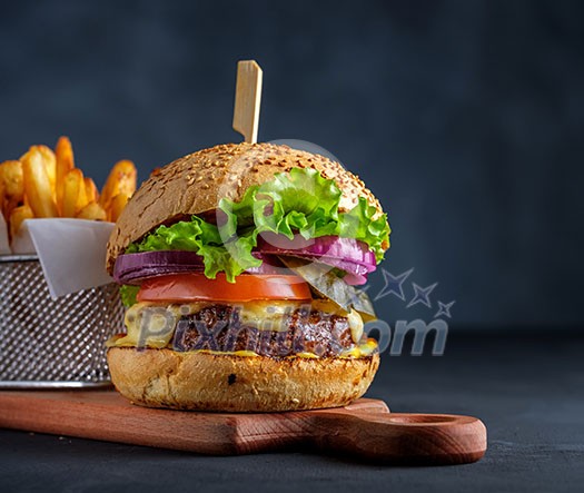 Tasty homemade grilled beef burger with lettuce, cheese and onion served on cutting board on a black wooden table, with copyspace Tasty homemade grilled beef burger with lettuce, cheese and onion served on cutting board on a black wooden table, with copyspace