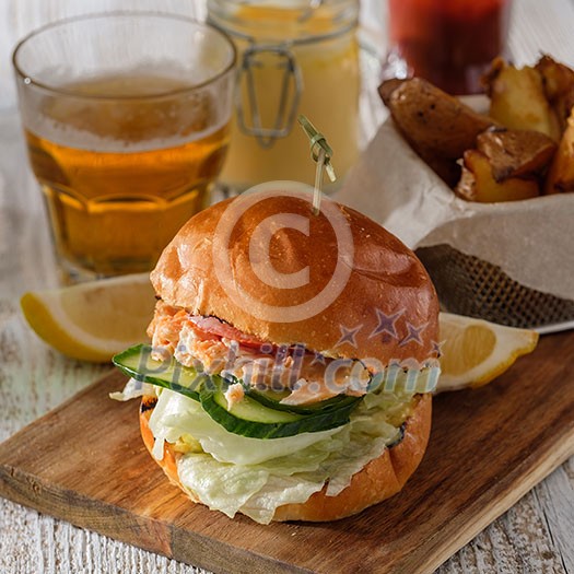 Fishburger with toppings, fries and a glass of beer. Rustic style. Fishburger with toppings, fries and a glass of beer. Rustic style.