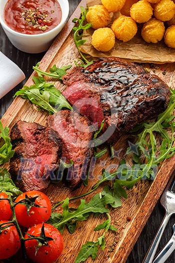 Juicy tasty grilled fillet steak served with tomatoes and cheese balls on an old wooden board Juicy tasty grilled fillet steak served with tomatoes and cheese balls on an old wooden board