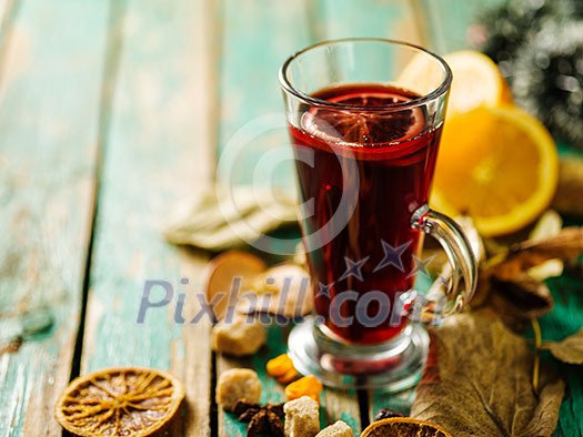 Hot mulled wine with orange, cinnamon, cardamom and anise on green wooden background.