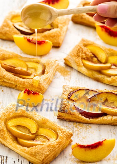 Tasty fresh homemade puff pastry with peach and honey on the white wooden table. Tasty fresh homemade puff pastry with peach and honey on the white wooden table.