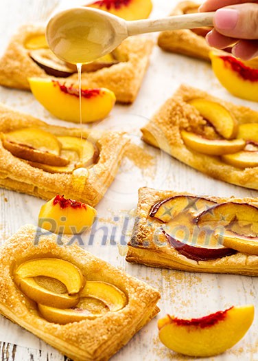 Tasty fresh homemade puff pastry with peach and honey on the white wooden table.