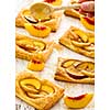 Tasty fresh homemade puff pastry with peach and honey on the white wooden table.