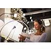 Pretty, young woman choosing the right light for her apartment in a modern home furnishings store (color toned image; shallow DOF)