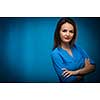 Pretty, young businesswoman with folded arms against blue background