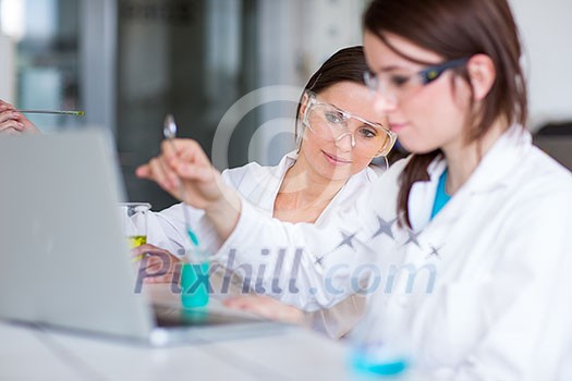 Two young female researchers carrying out experiments in a lab (shallow DOF; color toned image) Two young female researchers carrying out experiments in a lab (shallow DOF; color toned image)