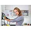 Senior woman cooking in the kitchen - eating and cooking healthy for her family; putting some potates in the oven, enjoying active retirement (shallow DOF; color toned image)