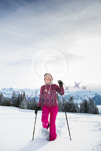 Pretty, young woman snowshoeing in high mountains, enjoying splendid winter weather with abundance of snow