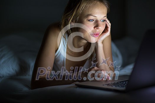 Pretty, young woman using her laptop computer in bed (color toned image; shallow DOF)