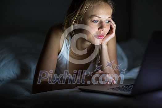 Pretty, young woman using her laptop computer in bed (color toned image; shallow DOF) Pretty, young woman using her laptop computer in bed (color toned image; shallow DOF)