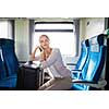 Pretty young woman traveling on a train with her big trunk (color toned image)