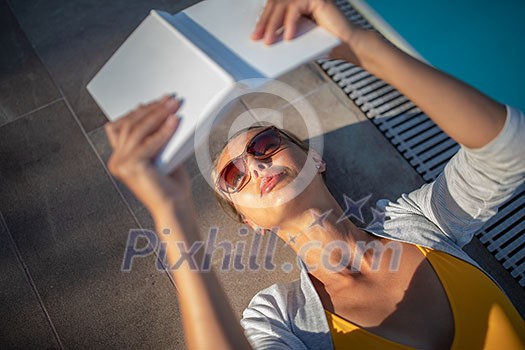 Young Beautiful Suntanned Woman wearing sunglasses relaxing next to a Swimming Pool on a lovely Summer Day - Reading a book Young Beautiful Suntanned Woman wearing sunglasses relaxing next to a Swimming Pool on a lovely Summer Day - Reading a book