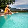 Young Beautiful Suntanned Woman wearing sunglasses relaxing next to a Swimming Pool  on a lovely Summer Day