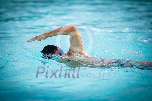 Man swimmer swimming crawl in a blue water pool. Portrait of an athletic young male triathlete swimming crawl wearing swimming goggles. Triathlete training for triathlon. Man swimmer swimming crawl in a blue water pool. Portrait of an athletic young male triathlete swimming crawl wearing swimming goggles. Triathlete training for triathlon.