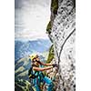 Pretty, female climber on a via ferrata -  climbing on a rock in Swiss Alps
