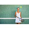 Portrait of a pretty, young, female tennis player in front of a training wall on a tennis court