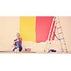 Portrait of a beautiful young female painter sitting on floor near wall after painting.