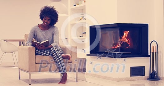 Young beautiful african american woman sitting in front of fireplace at home on a cold autumn day and reading book Young beautiful african american woman sitting in front of fireplace at home on a cold autumn day and reading book