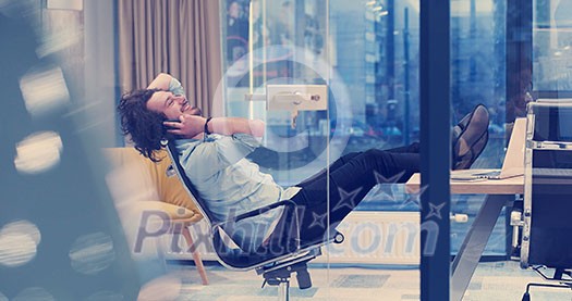Full length of a relaxed casual young businessman sitting with legs on desk at office Full length of a relaxed casual young businessman sitting with legs on desk at office