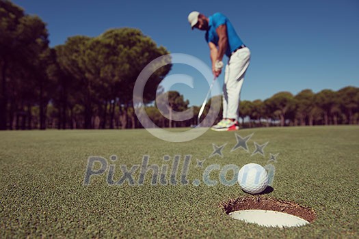 golf player hitting shot with driver, ball on edge of hole on course in background at beautiful sunny day golf player hitting shot with driver, ball on edge of hole on course in background at beautiful sunny day