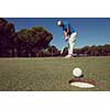 golf player hitting shot with driver, ball on edge of  hole  on course in background  at beautiful sunny day