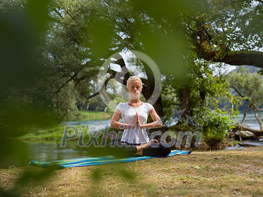 healthy woman relaxing while meditating and doing yoga exercise in the beautiful nature on the bank of the river