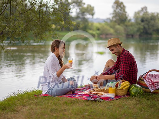 Couple in love enjoying picnic time drink and food in beautiful nature on the river bank Couple in love enjoying picnic time drink and food in beautiful nature on the river bank