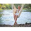 Young blonde woman resting on hammock while enjoying nature on the river bank