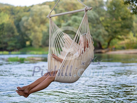 Young blonde woman resting on hammock while enjoying nature on the river bank Young blonde woman resting on hammock while enjoying nature on the river bank
