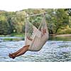 Young blonde woman resting on hammock while enjoying nature on the river bank