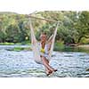 Young blonde woman resting on hammock while enjoying nature on the river bank