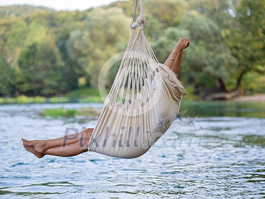 Young blonde woman resting on hammock while enjoying nature on the river bank Young blonde woman resting on hammock while enjoying nature on the river bank