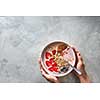 Light greek yogurt or cream dessert with almond flakes, oatmeal and fresh berry served in bowl in female hands on a concrete background, top view with space for text. Cleansing, diet, healthy food, fitness concept.