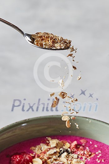Oat flakes are poured from a spoon into a plate with fresh fruit smoothies in a bowl. Preparation of a healthy breakfast