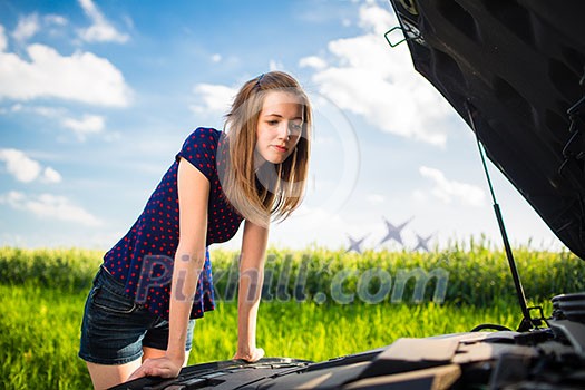 Pretty, young woman by the roadside after her car has broken down, inspecting the engine Pretty, young woman by the roadside after her car has broken down, inspecting the engine