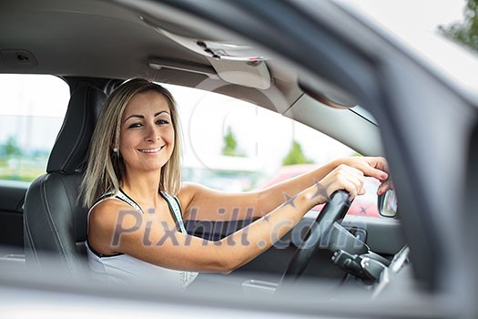 Woman driving a car - female driver at a wheel of a modern car, looking happy, smiling with a relaxed smile (shallow DOF; color toned image) Woman driving a car - female driver at a wheel of a modern car, looking happy, smiling with a relaxed smile (shallow DOF; color toned image)