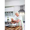 Senior woman cooking in the kitchen - eating and cooking healthy for her family; putting some potates in the oven, enjoying active retirement (shallow DOF; color toned image)