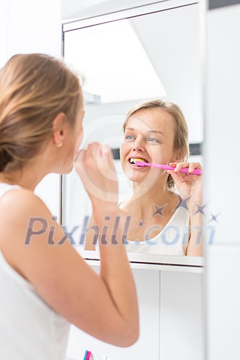 Pretty female brushing her teeth in front of mirror in the morning Pretty female brushing her teeth in front of mirror in the morning