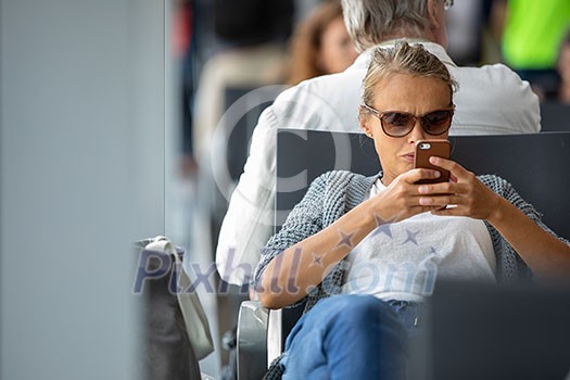 Casual blond young woman using her cell phone while waiting to board a plane at departure gates at international airport. Casual blond young woman using her cell phone while waiting to board a plane at departure gates at international airport.