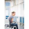 Female patient, sitting in a wheelchair for patients feeling not well enough to stand, waiting to be taken care of in a modern hospital (shallow DOF; color toned image)